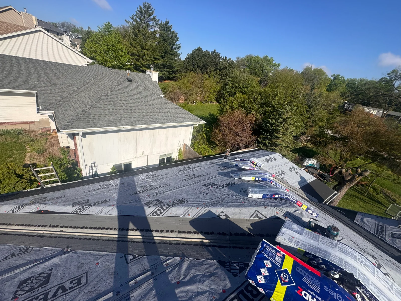 Synthetic underlayment and GAF Timberline HDZ shingle bundles staged on a roof deck during replacement
